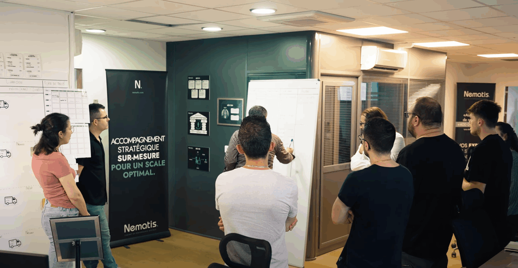 Équipe Nematis échange autour d'un tableau blanc, outils digitaux et bannière visibles dans le bureau moderne.