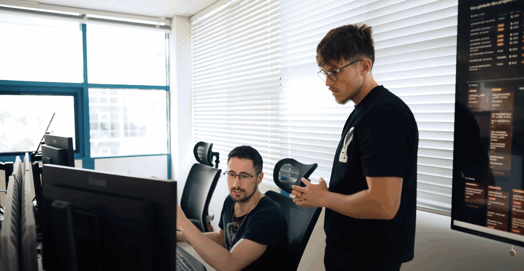 Deux hommes discutent stratégie digitale dans un bureau moderne lumineux, concentrés devant plusieurs écrans.