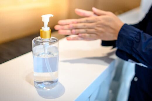 Flacon de gel désinfectant sur table, personne appliquant, environnement propre et lumineux.